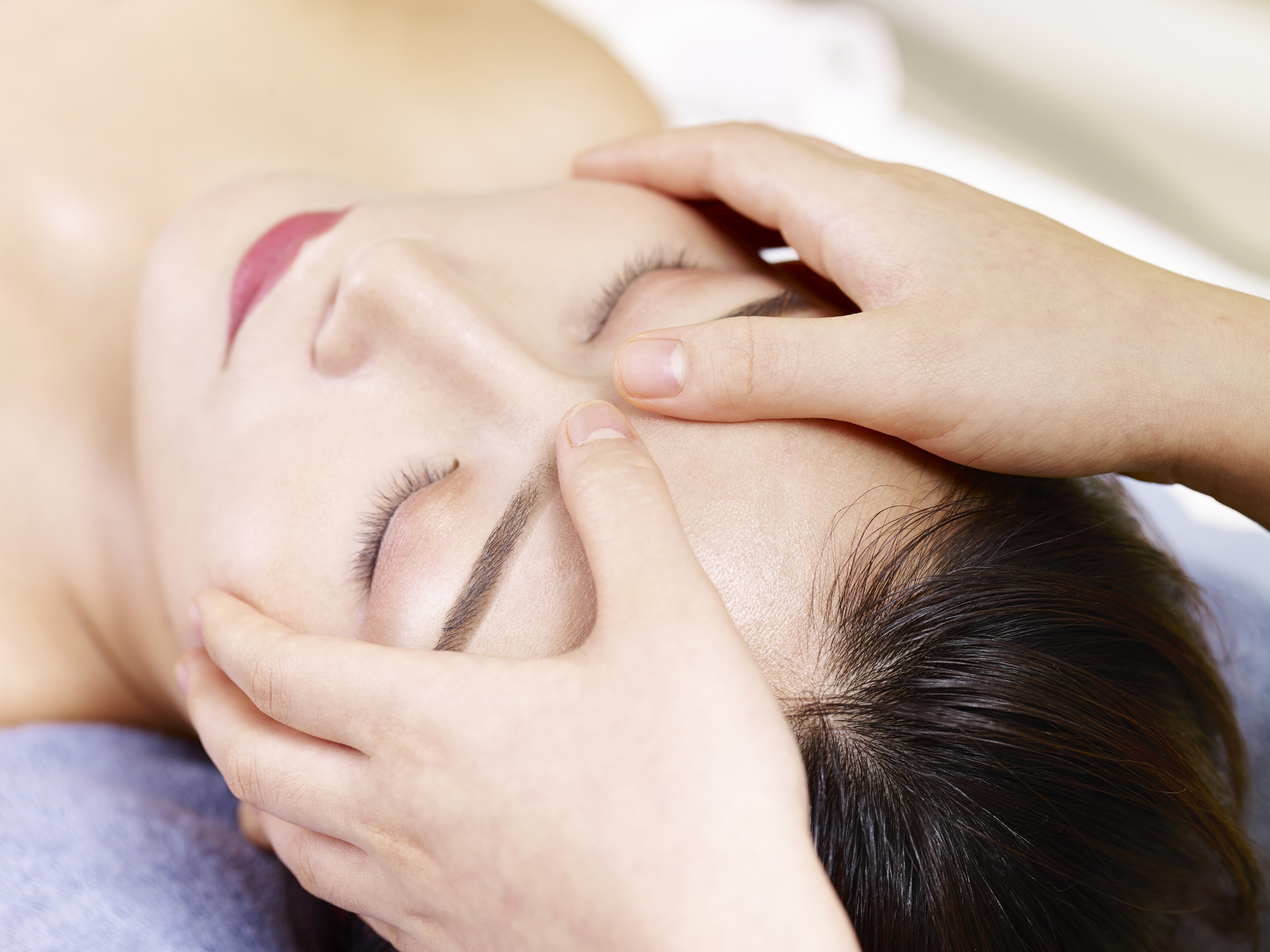 Young Asian woman receiving face massage in spa salon.